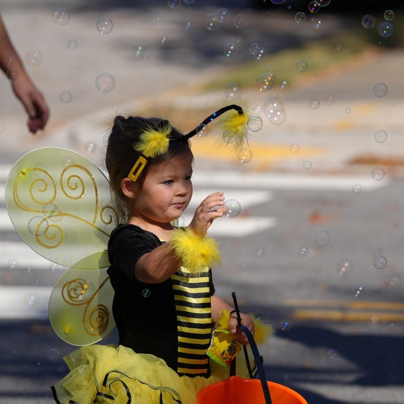 girl in bee costume pops bubbles while holding candy and bucket